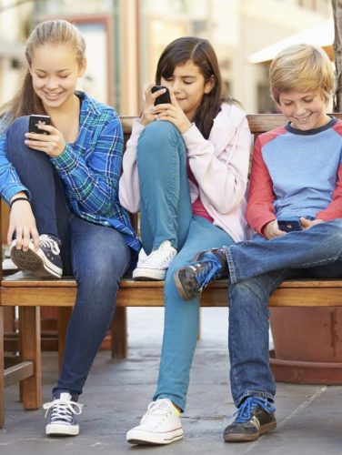 Group Of Children Sitting In Mall Using Mobile Phones